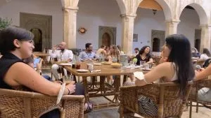 Un grupo de asistentes conversa alrededor de mesas de madera en el claustro del monasterio, bajo los arcos de piedra.
