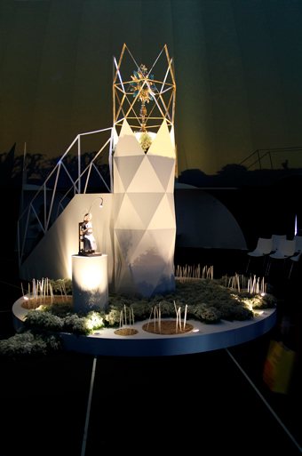 El faro eucarístico de noche, con la custodia en lo alto y velas encendidas a sus pies.