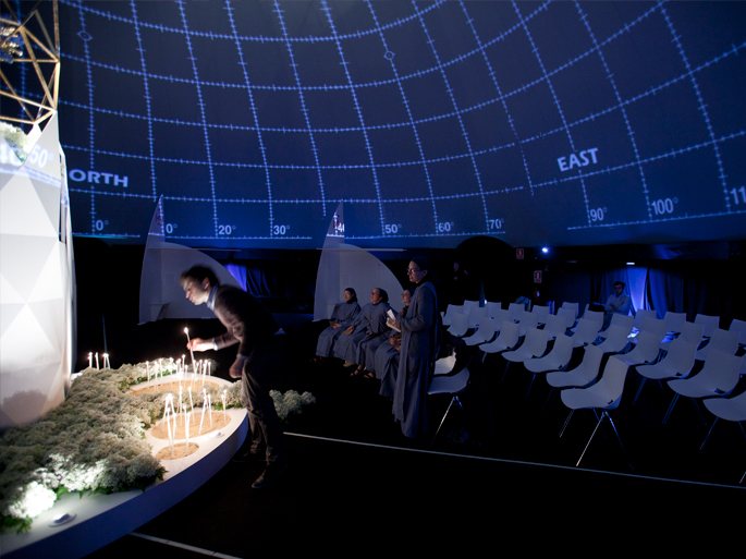 Interior del domo bajo la cúpula iluminada en azul, con los fieles en oración ante el faro.