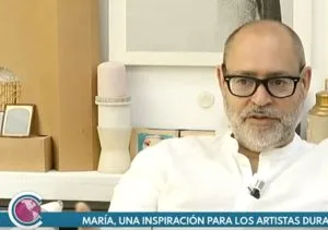 Fotograma de la entrevista en televisión: Javier Viver, sentado en su estudio, con el rótulo «María, una inspiración para los artistas».