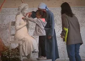 Varias religiosas, junto a un niño, tocan la talla sedente de la Bella Pastora en el taller.