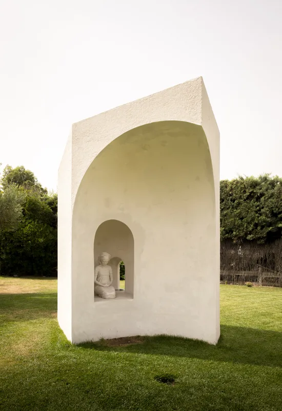 La Ermita de Lola en el jardín: un volumen encalado de cubierta apuntada, con un gran arco abierto y, en su hornacina, la figura sedente de la Virgen.