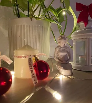 La miniatura de la Virgen entre bolas de Navidad rojas, una vela de Adviento y luces encendidas.
