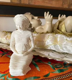 La miniatura de la Virgen, arrodillada ante la figura del Niño reclinado sobre un mantel bordado.