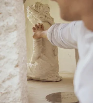 Una mano posada sobre la escultura de la Virgen, dentro de la ermita de piedra encalada.
