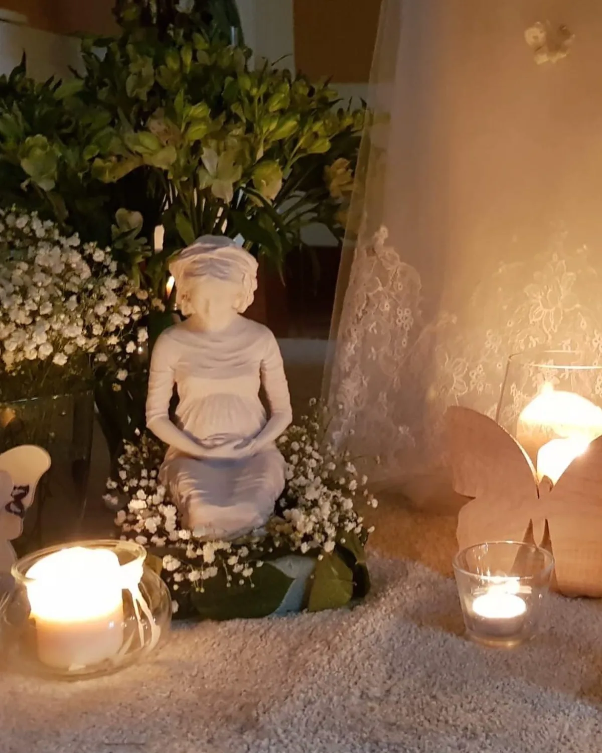 La Virgen de Hakuna en un altar doméstico, entre velas encendidas, paniculata y un ramo de flores.