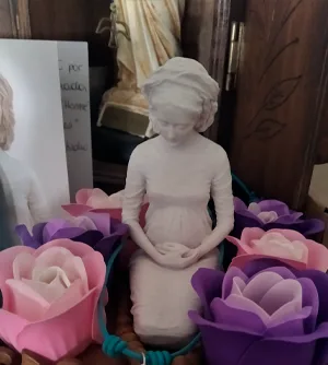 La Virgen de Hakuna sentada, rodeada de flores de papel en tonos rosa y morado.
